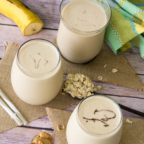This picture is 3 glasses of peanut punch with a banana and some oats on the side.