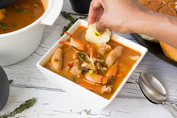 A picture of a hand dipping bread into a bowl of seafood soup