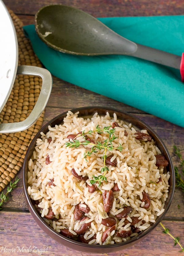 A bowl of rice and peas with a pot of rice and peas  in the background.