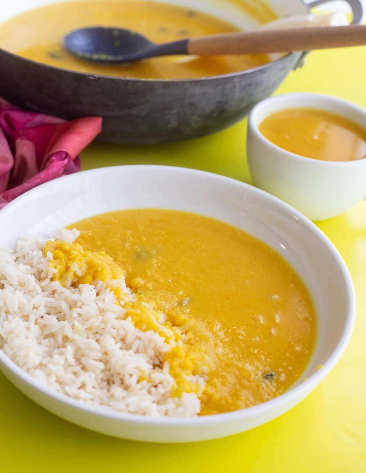 Yellow split peas dhal on top of white rice in a white bowl with more dhal in the back ground.