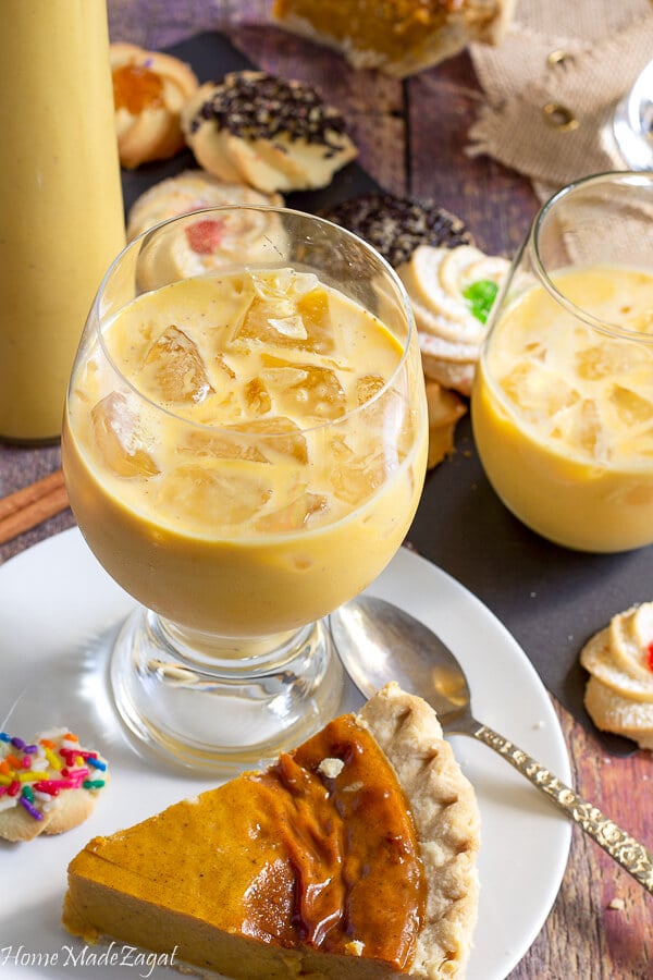 A close up of a glass of ice with ponche de creme with other desserts in the back ground
