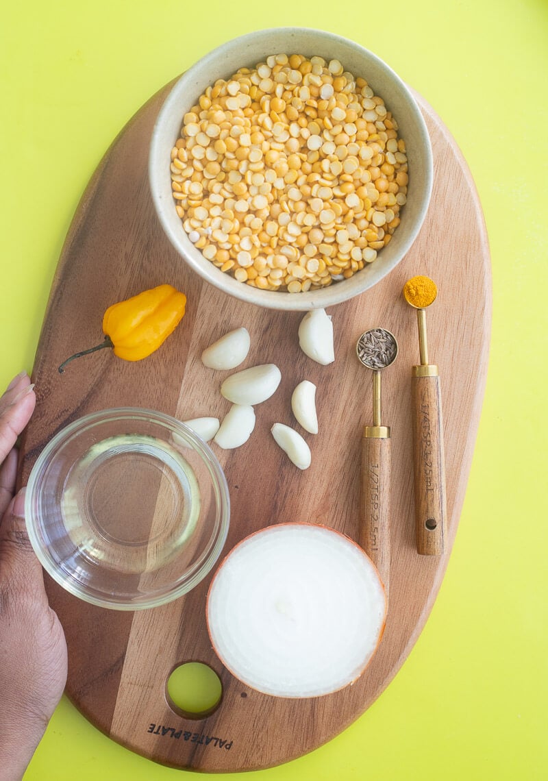 Ingredients for Trinidadian dhal and rice recipe, including split peas, garlic, onions, cumin, turmeric, and white rice, laid out on a serving board..