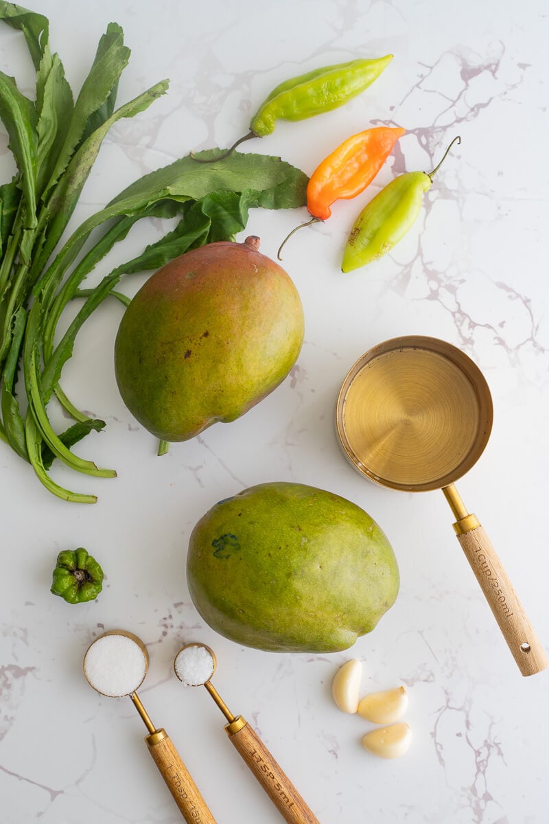 Ingredients needed to make mango chutney on a white backdrop.