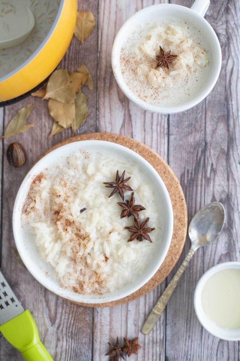 A bowl of creamy rice porridge topped with aniseed and grated nutmeg in a white bowl.
