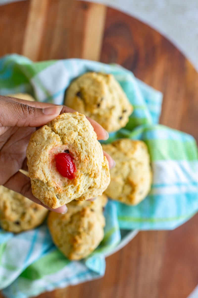 A hand holding baked rock buns with a cherrie in the middle of one.