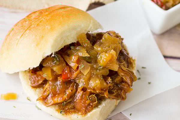 Jerk chicken sandwich on a white sheet topped with pineapple chutney.