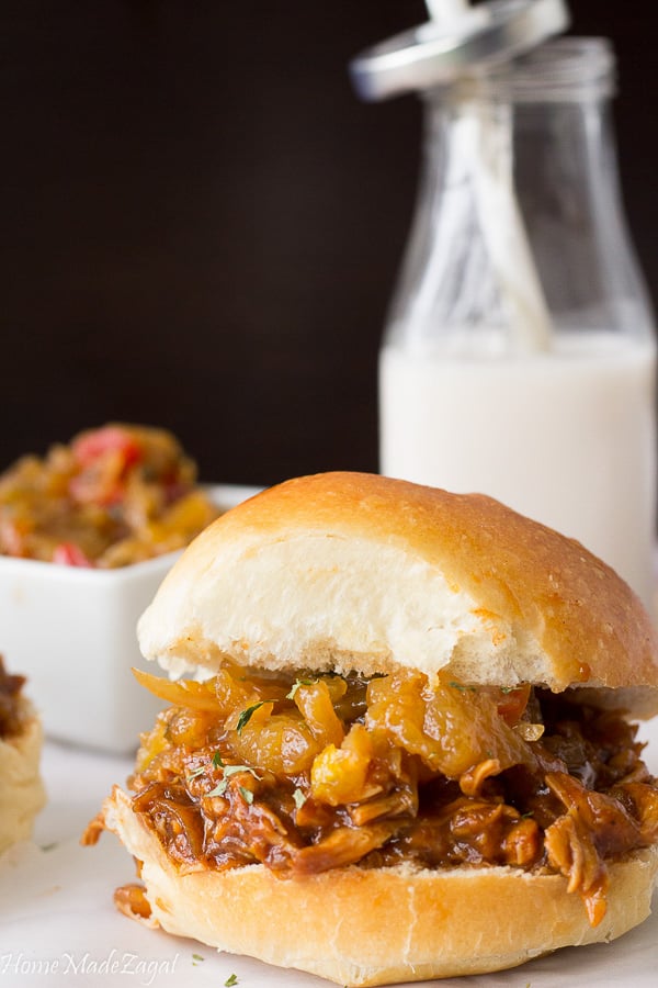 A jerk chicken sandwich close up with a bottle of milk in the background.