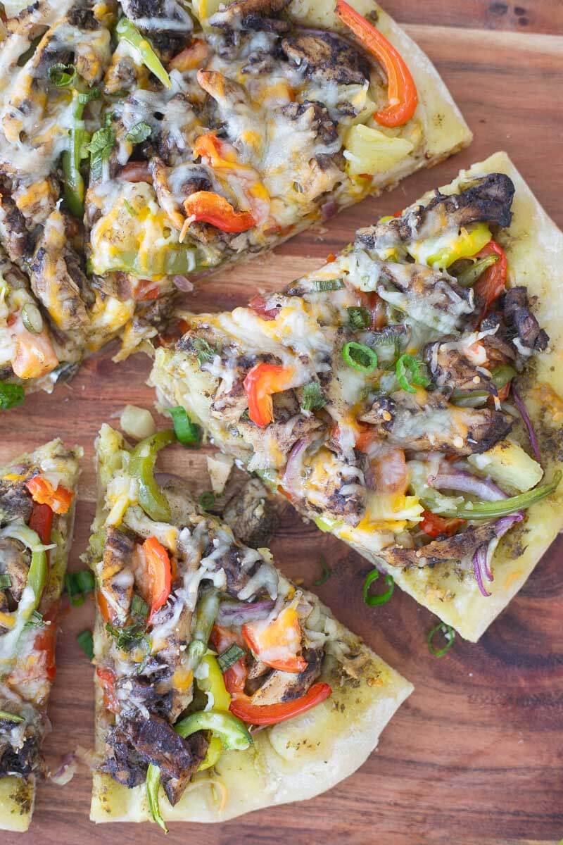 Close up of the slices of jerk pizza seeing all the tomatoes, and peppers and jerk chicken.