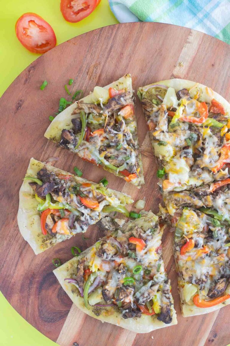 Slices of jerk chicken pizza, on a brown serving board on top of a green surface.