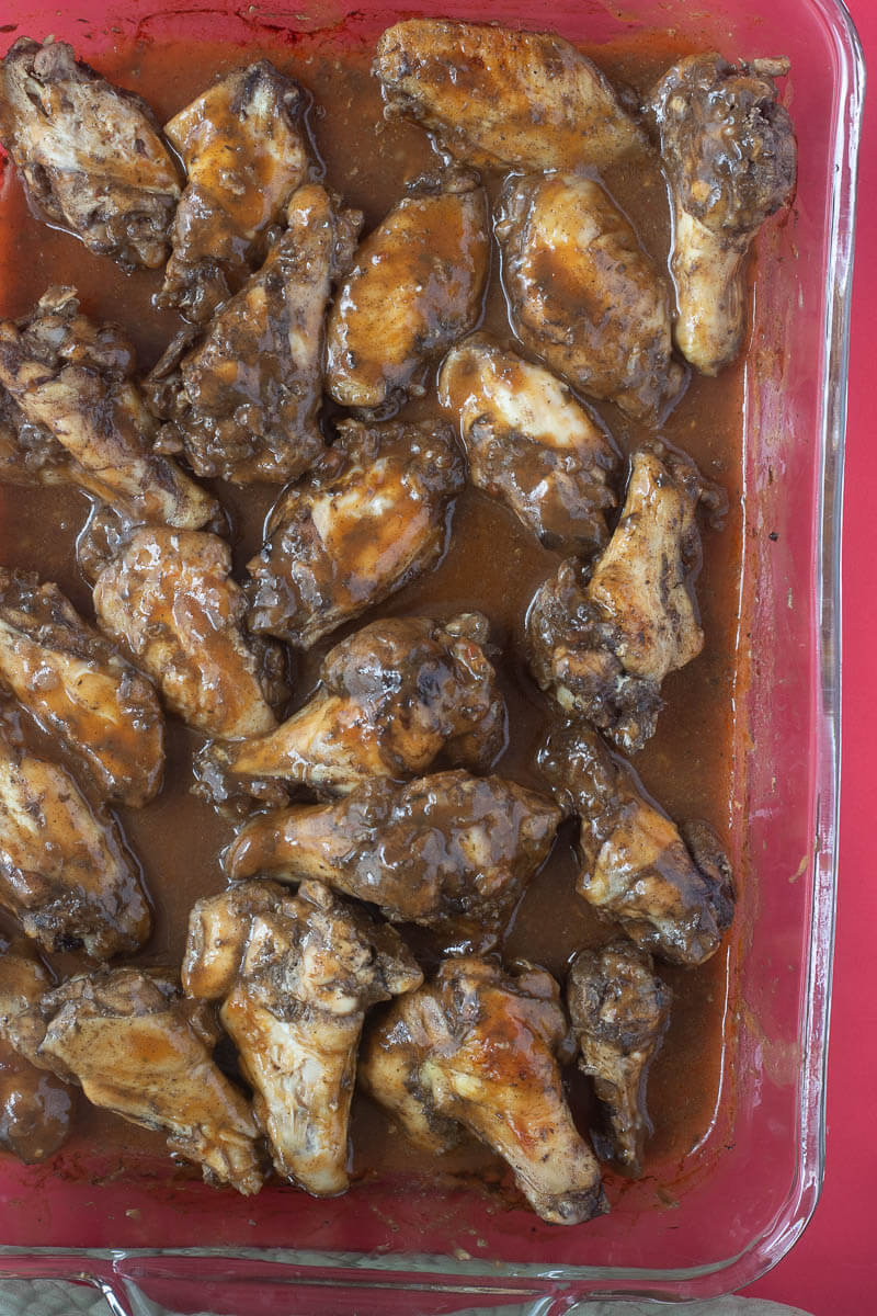 Baked jerk wings with BBQ sauce in a baking tray.