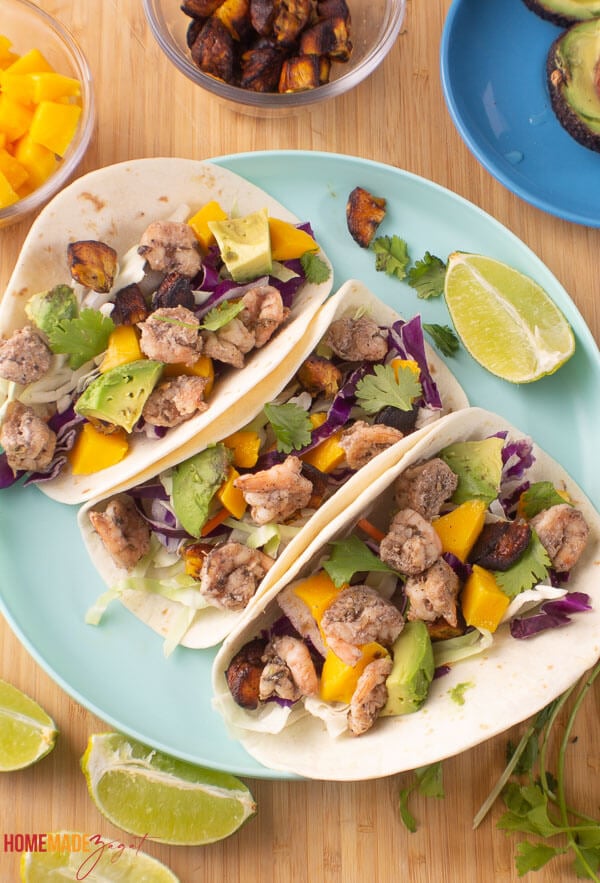 Three jerk shrimp tacos with toppings of mango salsa, plantains and fresh cilantro sprinkled.