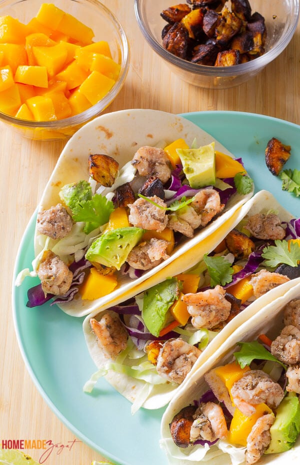 Jerk shrimp tacos on a blue plate with mango and sweet plantains.