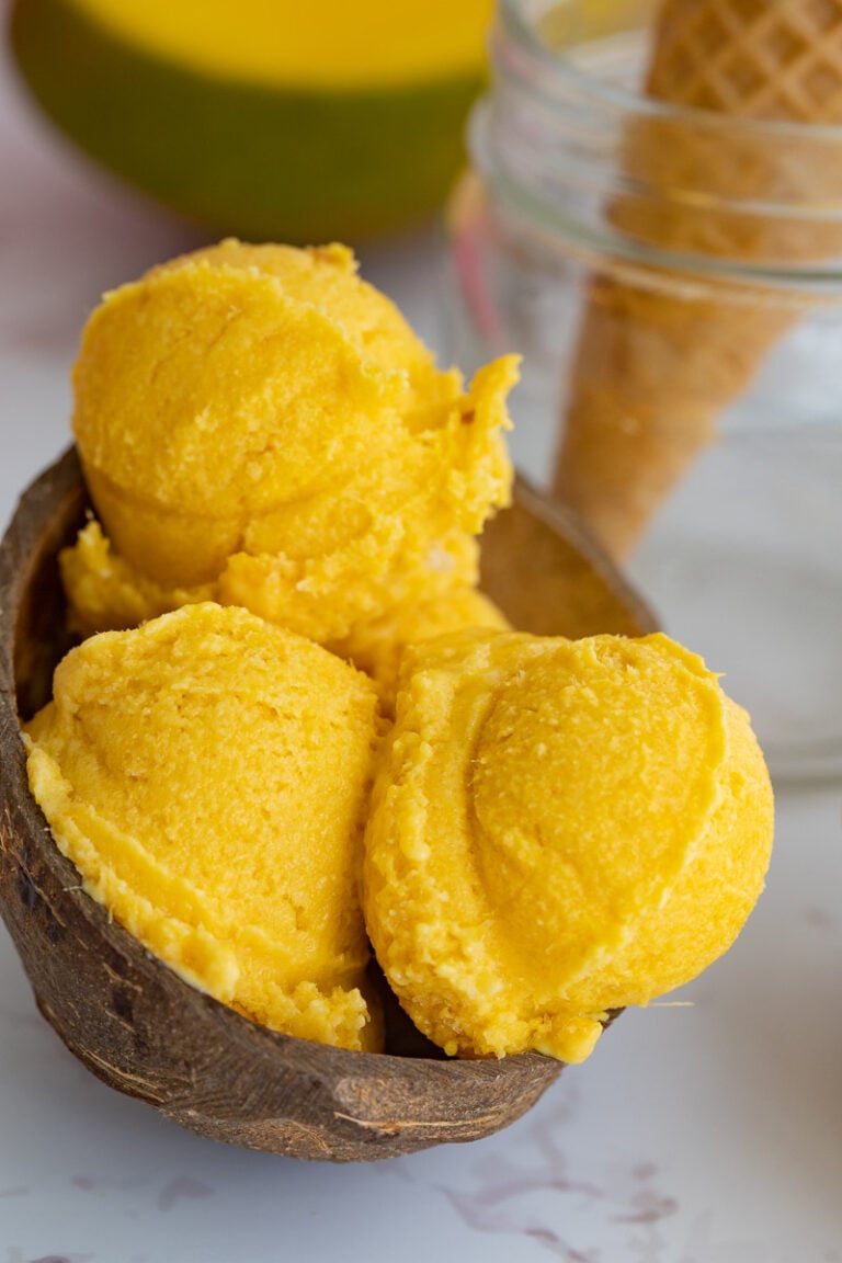 A picture of three scoops of mango ice cream with condensed milk in a coconut bowl.