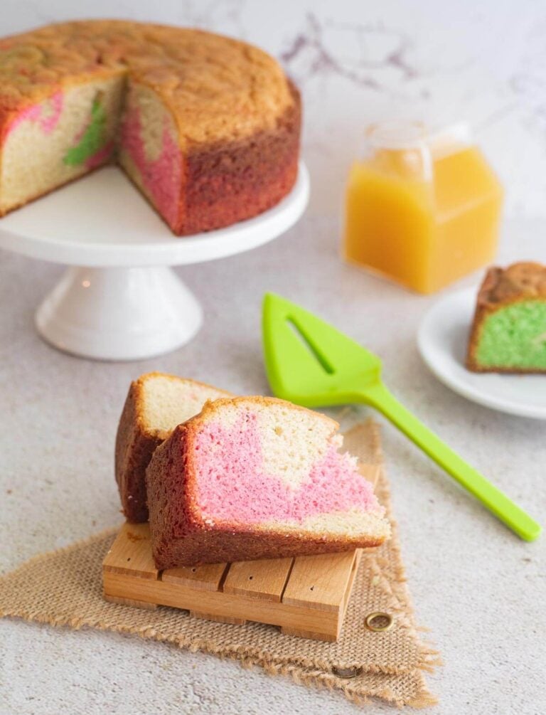 A slice of marble sponge cake on a plate showing the marble with the remaining cake in the background.