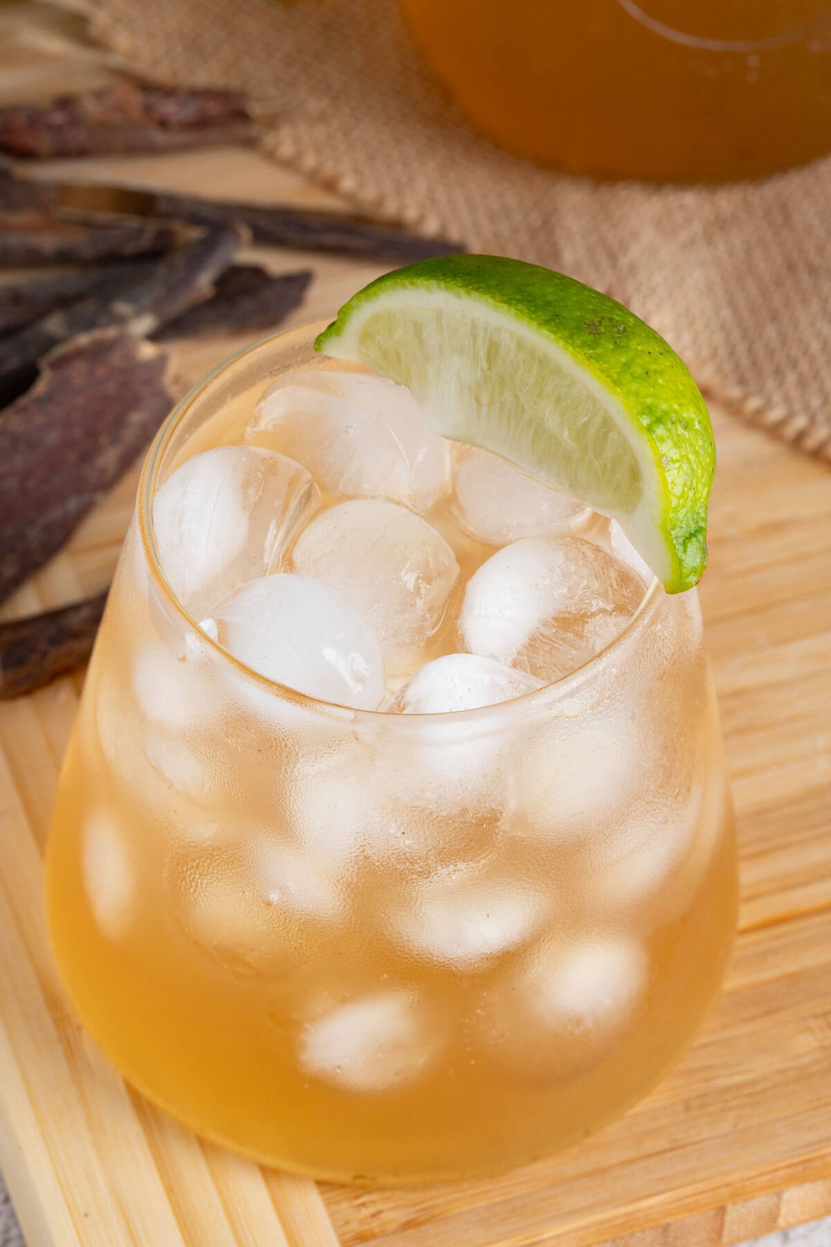 Close up of a glass of mauby on ice with a slice of lime resting on the top.