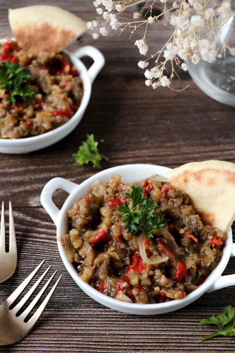 Two bowls of baigan choka with naan bread on the side.