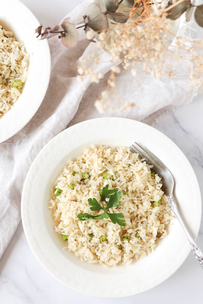 A white plate of ochro and rice with a garnish.