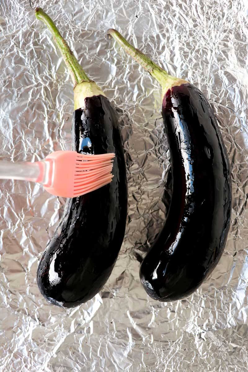 Eggplants being coated with coconut oil on foil sheets.