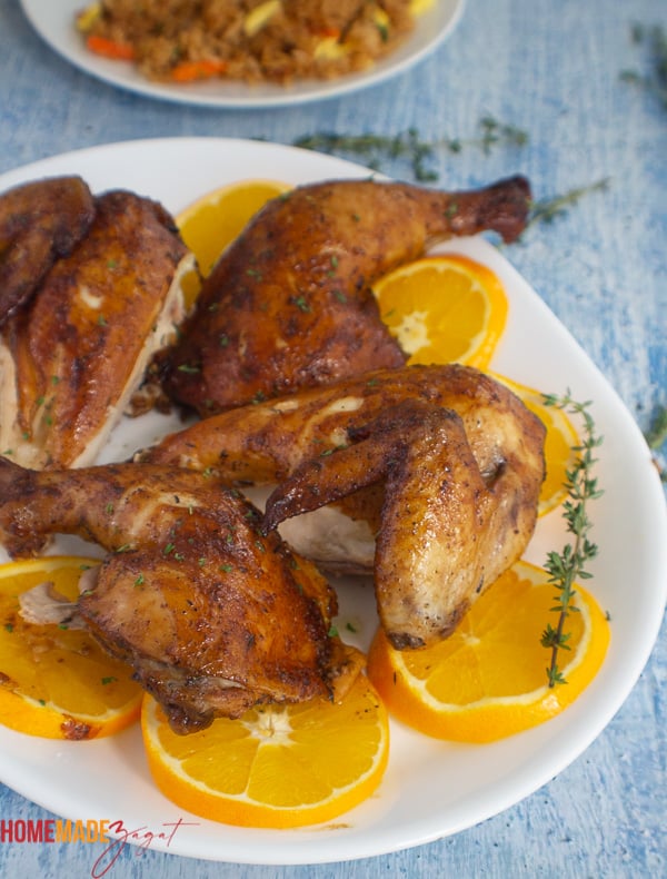A plate of roasted orange ginger chicken, cut up in parts on a plate of orange slices.