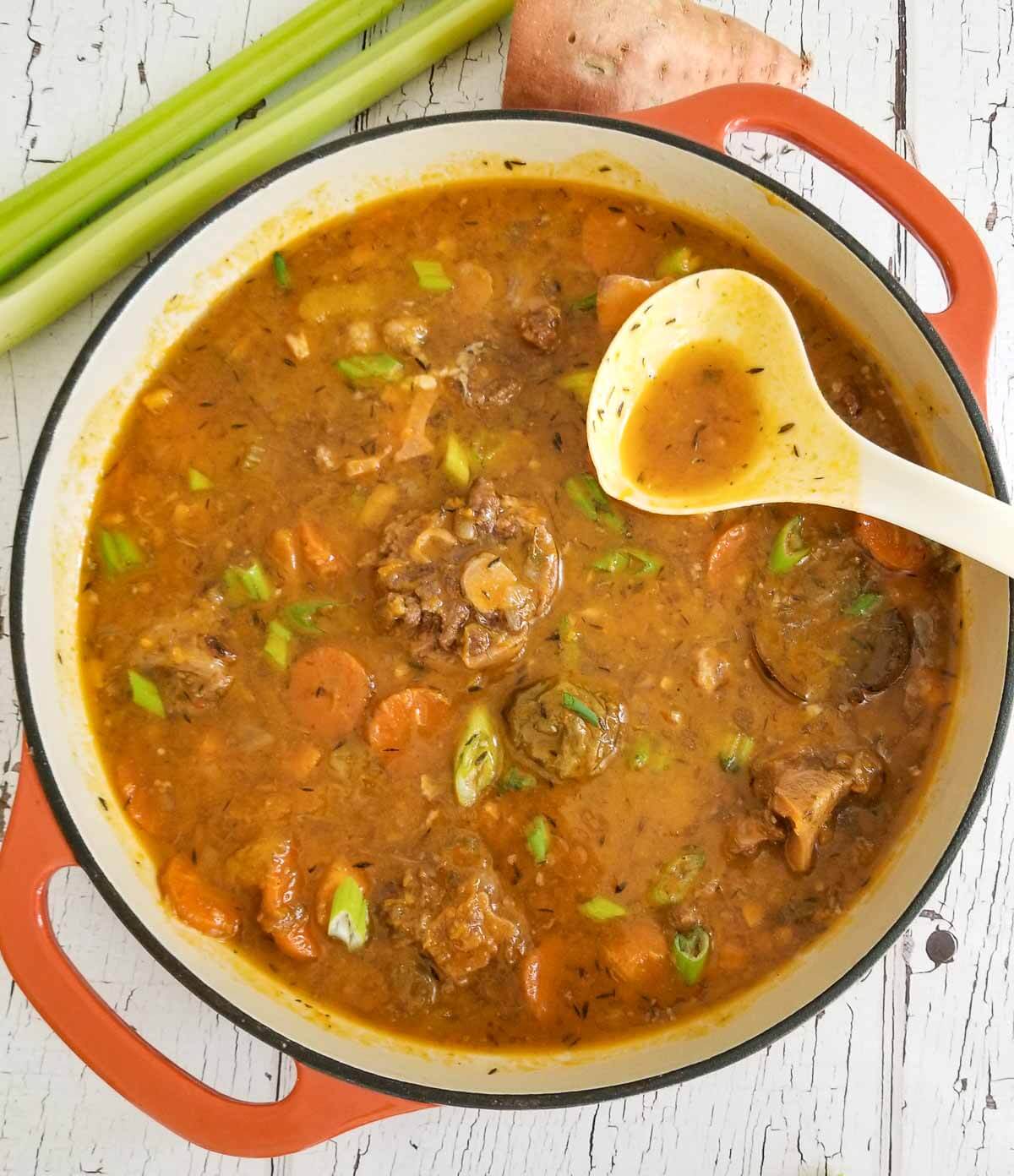 Pot of finished oxtail soup made in the slow cooker served in a wide dutch pot.