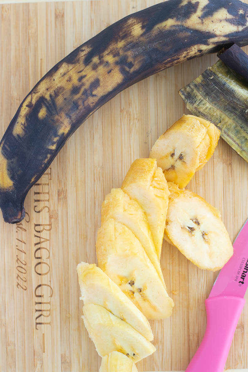 Ripe plantain sliced on a cutting board with a pink knife.