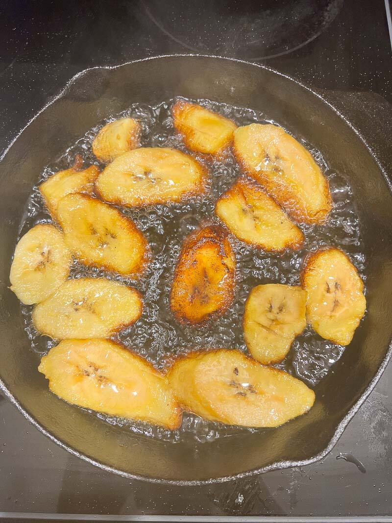Jamaican style plantains being fried in a cast iron skillet.