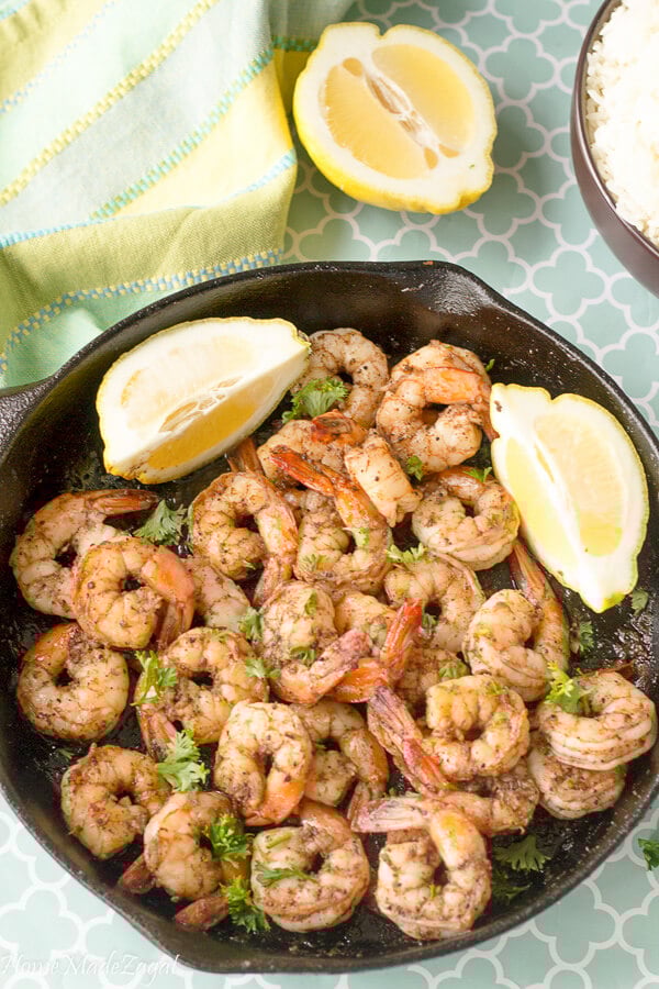 A cast iron pot full of cooked jerk shrimp with slices of fresh limes.