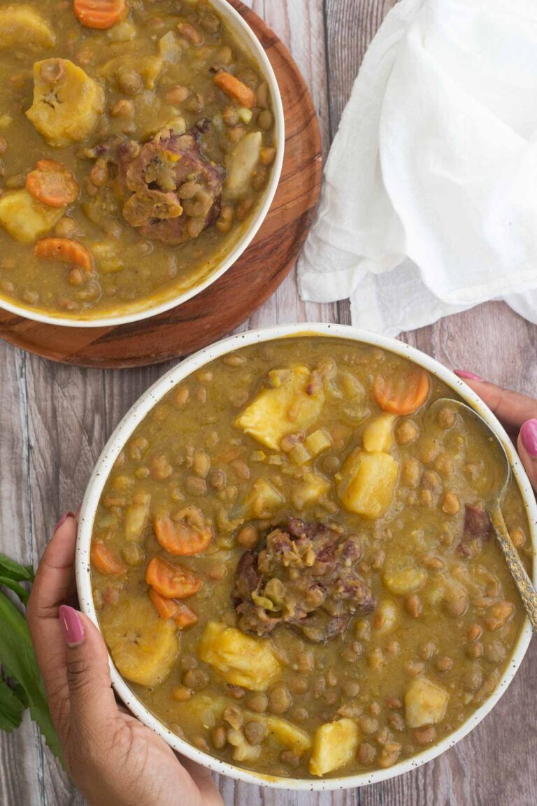 Top view of two bowls of pigeon peas soup on a brown serving plate with hands holding a bowl.