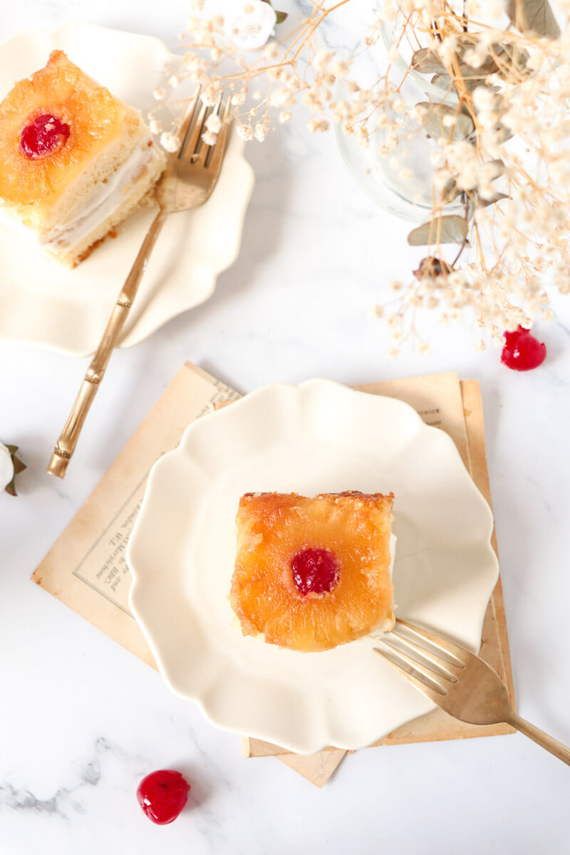 Slices of 2-layered pineapple cake on white plates with forks.
