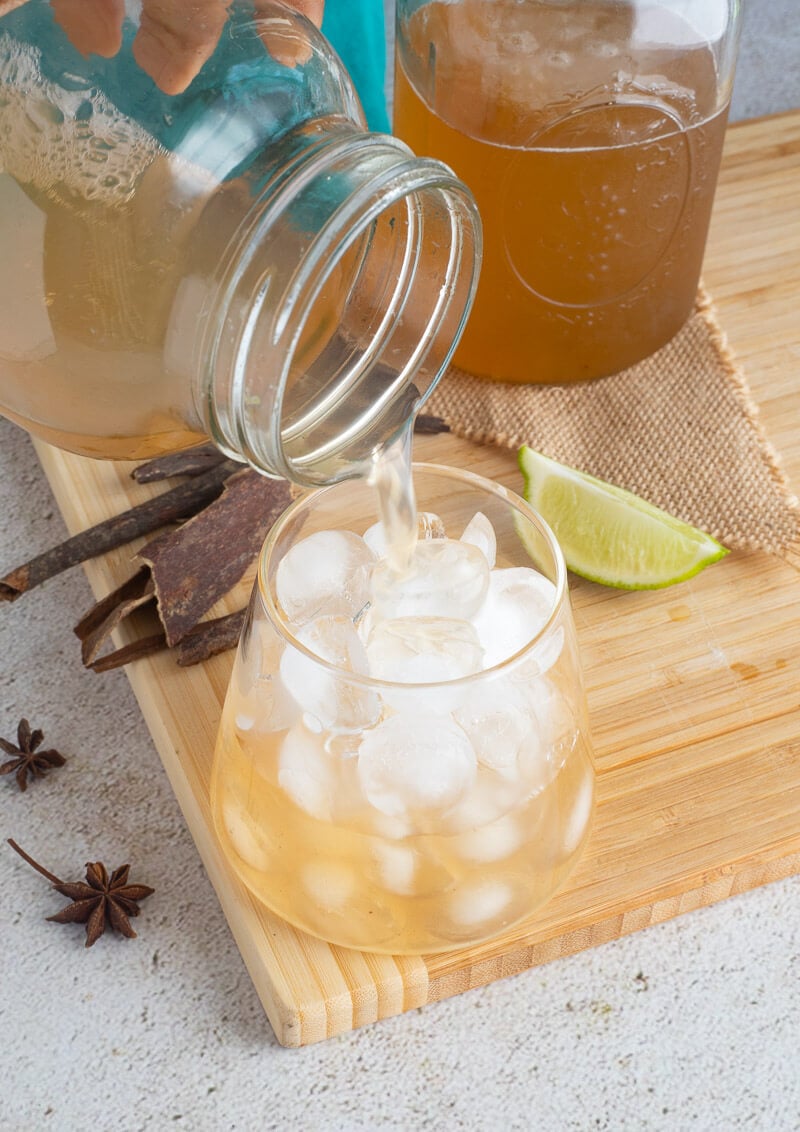 Pouring out of mauby from a mason jar into a glass of ice.