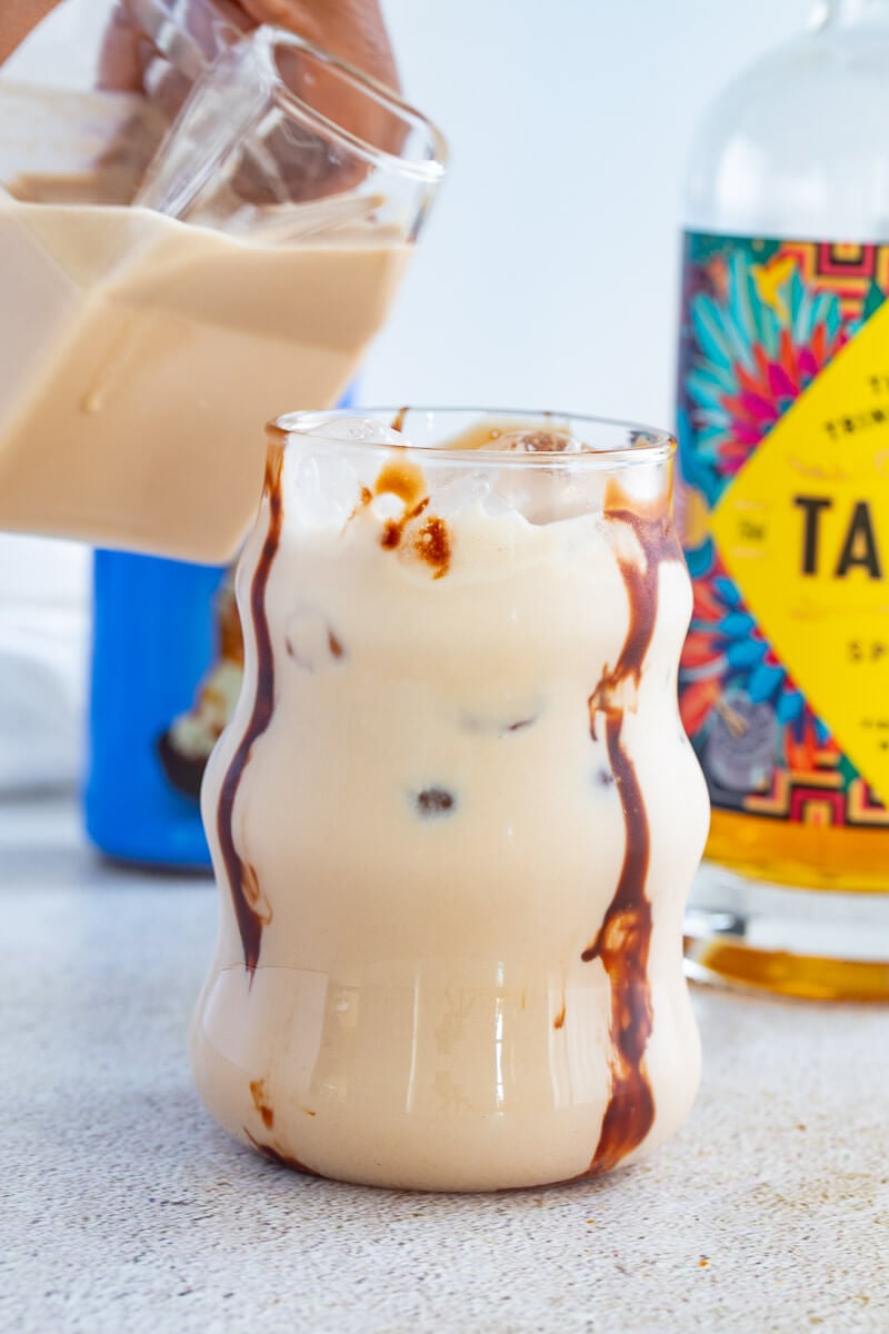 Finshed rum creme in a glass with ice and chocolate drizzles as a garnish.