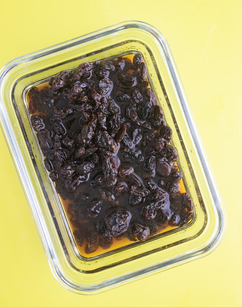 Raisins soaking in dark rum in a glass bowl.
