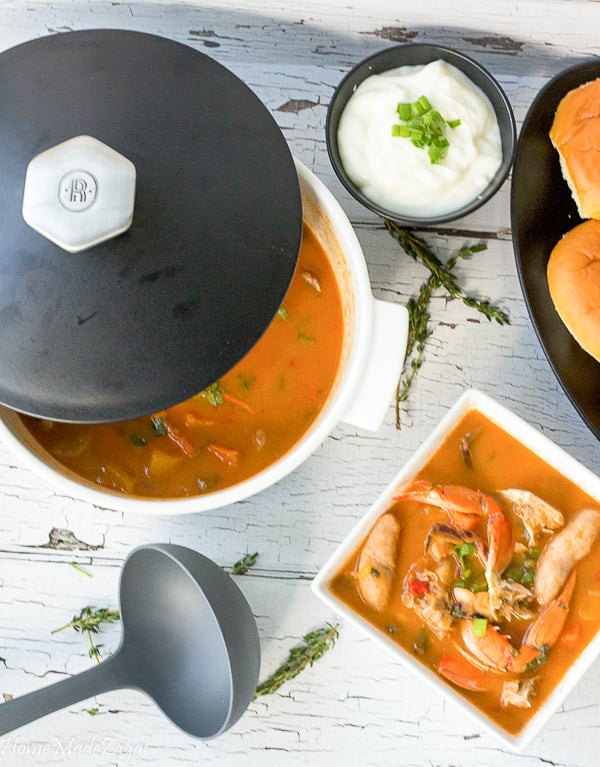 A dutch pot and a bowl filled with seafood soup and a serving spoon