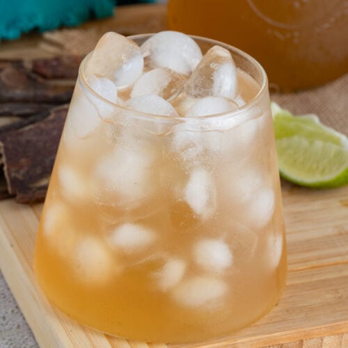 Chilled sweetened mauby in a glass on a brown board.