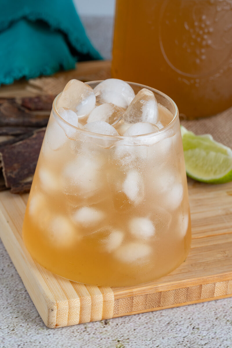 Chilled sweetened mauby in a glass on a brown board.