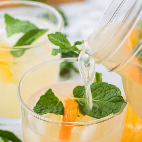 Pouring punch into a glass of ice with mint and orange slices