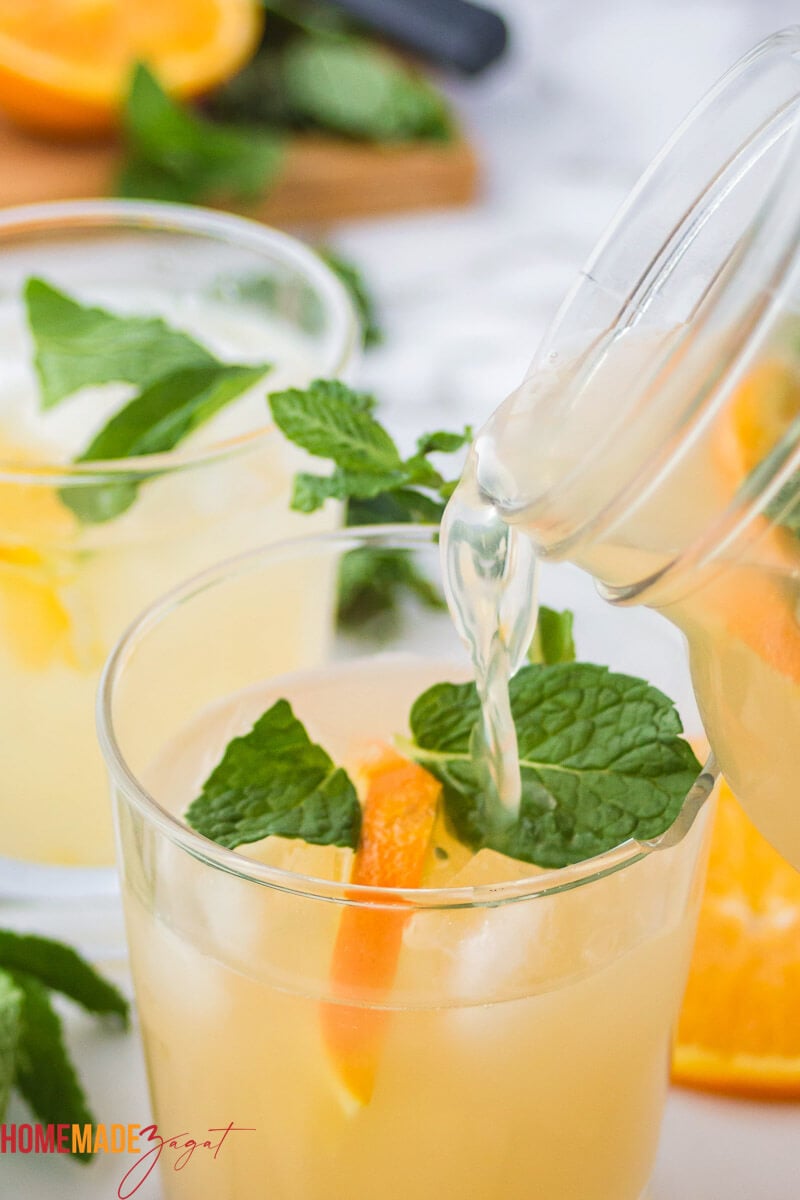 Pouring punch into a glass of ice with mint and orange slices