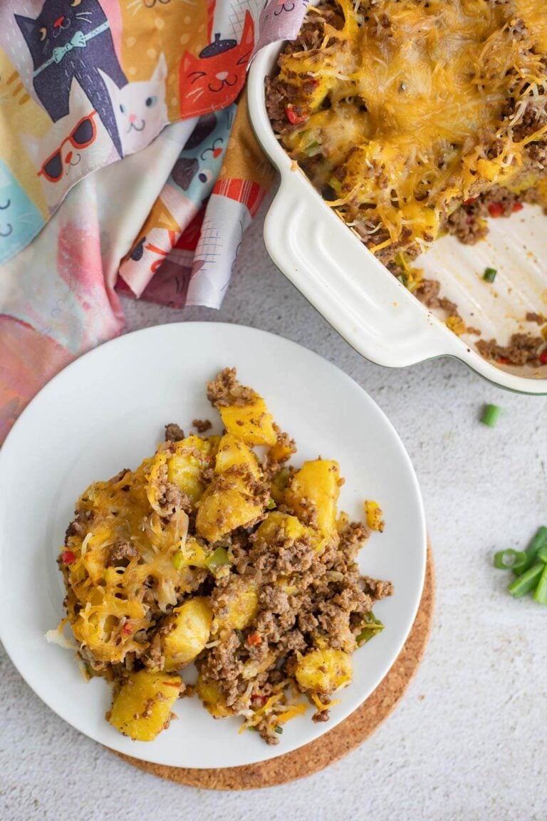 A serving of ripe plantain pie on a white plate with a casserole dish of pie in the background.