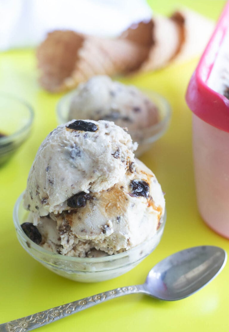 Three scoops of rum and raisin ice cream in a glass bowl with waffles cones in the backgound.