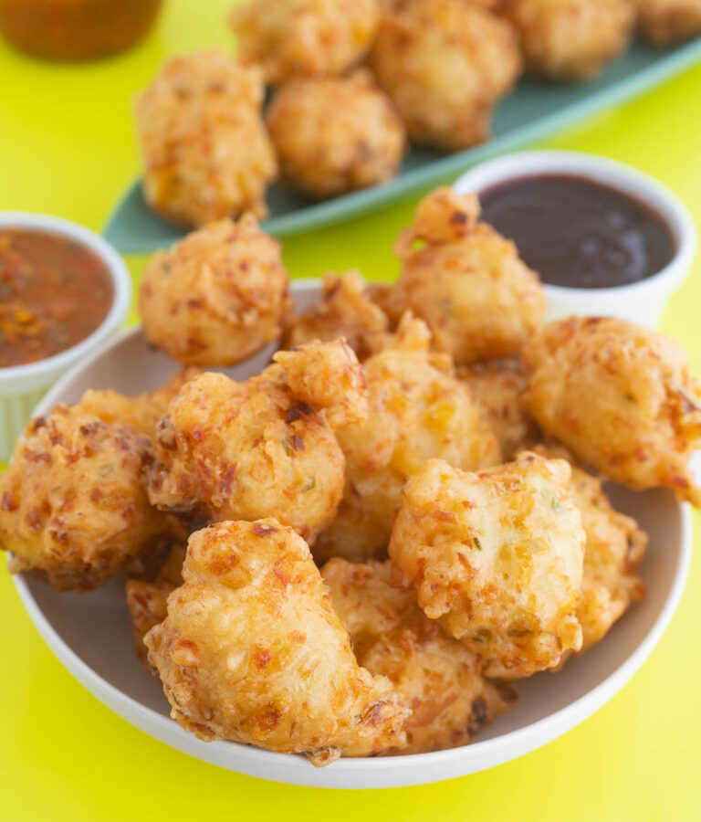 A bowl full of fried saltfish accras with a pepper dip in the background.
