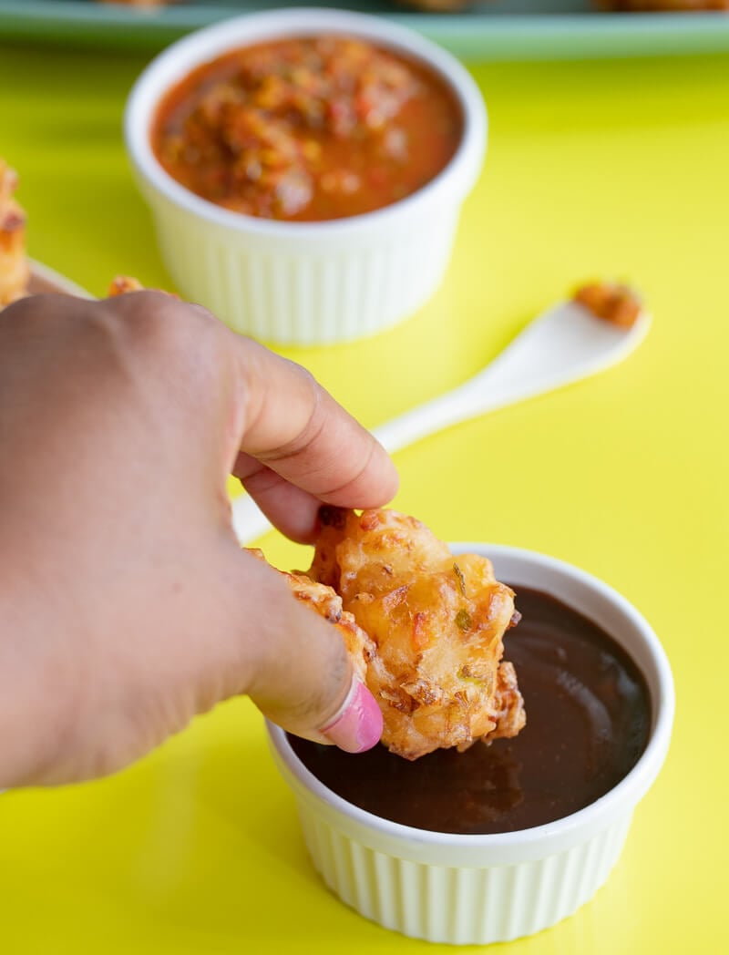 A picture of a hand dipping accra into some tamarind chutney.