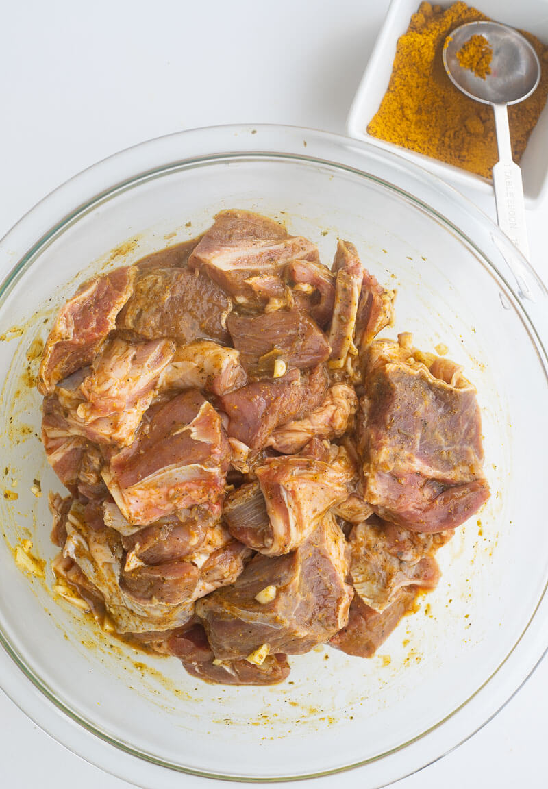 Seasoned goat meat and a bowl of curry powder on a white countertop.