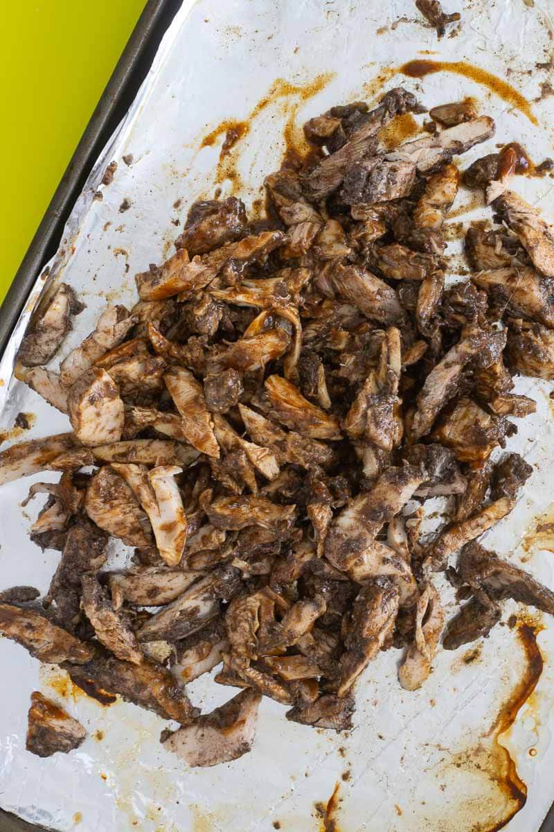 Shredded jerk chicken with jerk bbq sauce on a baking sheet.