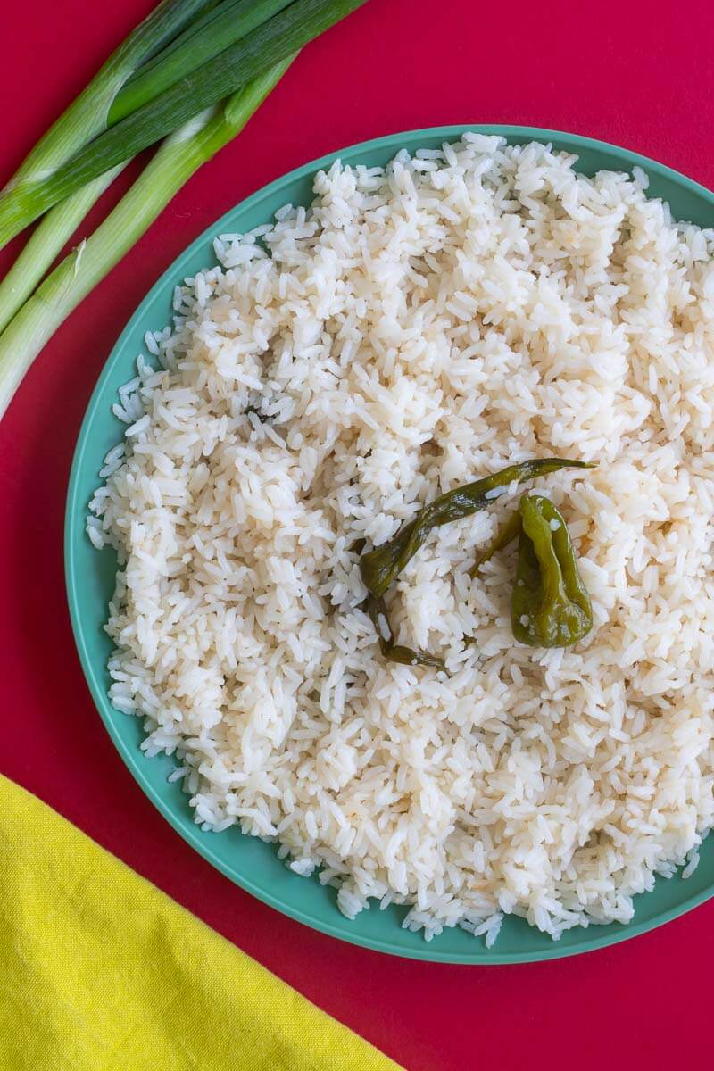 Steamed rice on a green plate with pepper and scallion on top a red counter.