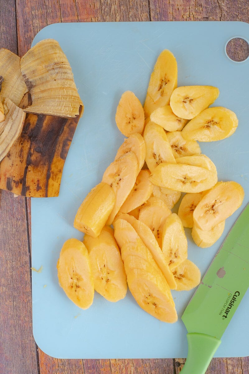 Ripe plantains sliced up on a cutting board with plantain skin on the side,