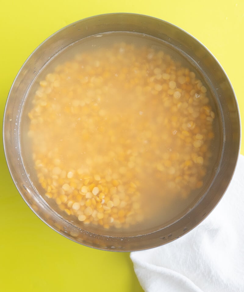 Yellow split peas covered in water soaking in a metal bowl on a countertop.