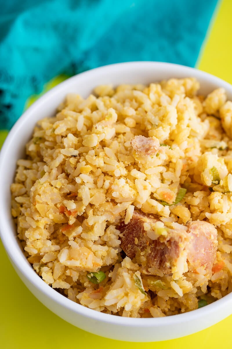 Split peas and rice in a white bowl with a piece of smoked bones on top. A green napkin in the background.