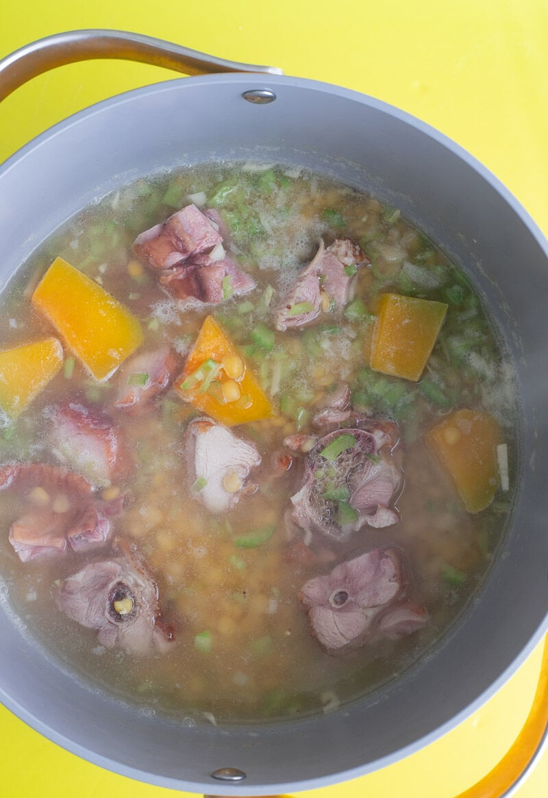 A large pot with fresh split peas, smoked bones, pumpkin, water and aromatics.