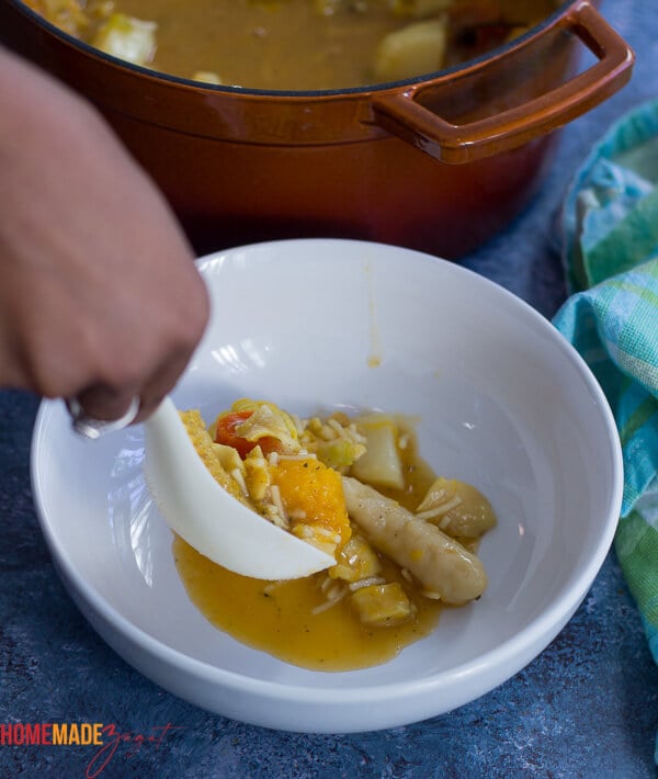 Spooning out of soup into a white bowl on a blue background.