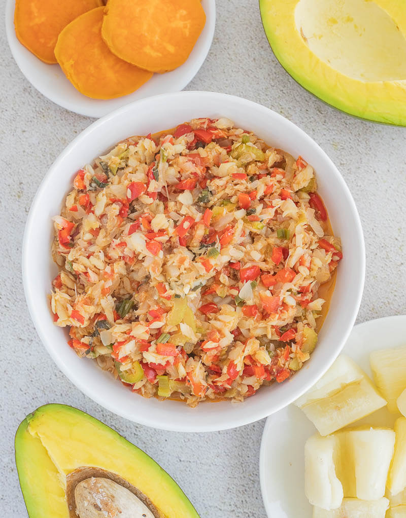 A bowl of stewed saltfish and individual plates of ground provisions and avocado.